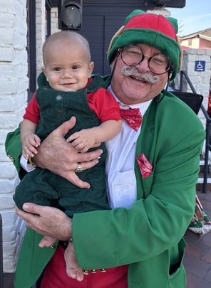 Godfrey the Magic Elf holding a smiling baby dressed in a matching green elf outfit