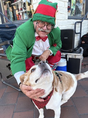 Godfrey the Magic Elf affectionately holding the face of a happy dog wearing a bandana