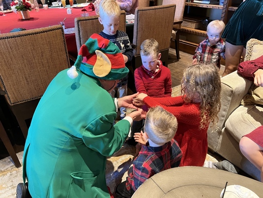 A group of children gathered closely around Godfrey the Magic Elf as he performs magic