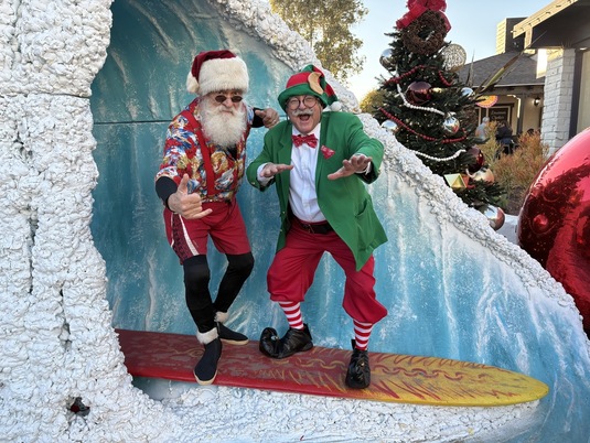 Surfin Santa and Godfrey the Magic Elf posing on a surfboard in front of a holiday wave display